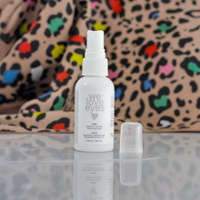 Load image into Gallery viewer, White spray bottle labeled 'we love eyes' on a reflective surface with a colorful leopard print background.