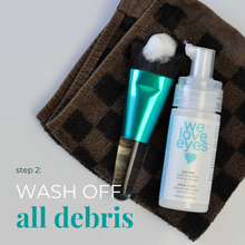 Load image into Gallery viewer, Makeup brush and bottle labeled 'we love eyes' on a brown checkered towel with text 'WASH OFF all debris'.