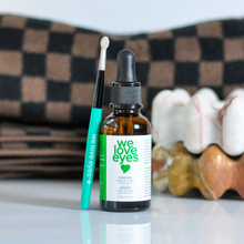 Load image into Gallery viewer, Bottle of 'we love eyes' eye serum with applicator on a checkered fabric background