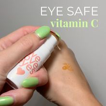 Load image into Gallery viewer, Hand holding a 'EYE SAFE vitamin C' product with a swatch on skin against a gray background