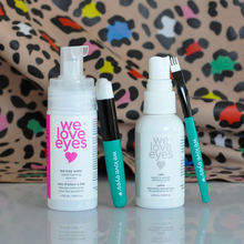 Load image into Gallery viewer, Two 'we love eyes' eye care products with applicators on a reflective surface with a colorful patterned background.
